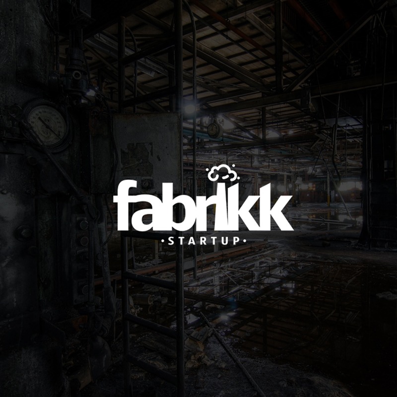Białe logo 'fabriikk STARTUP' na tle ciemnego, opuszczonego wnętrza fabryki z metalowymi konstrukcjami i rurami.