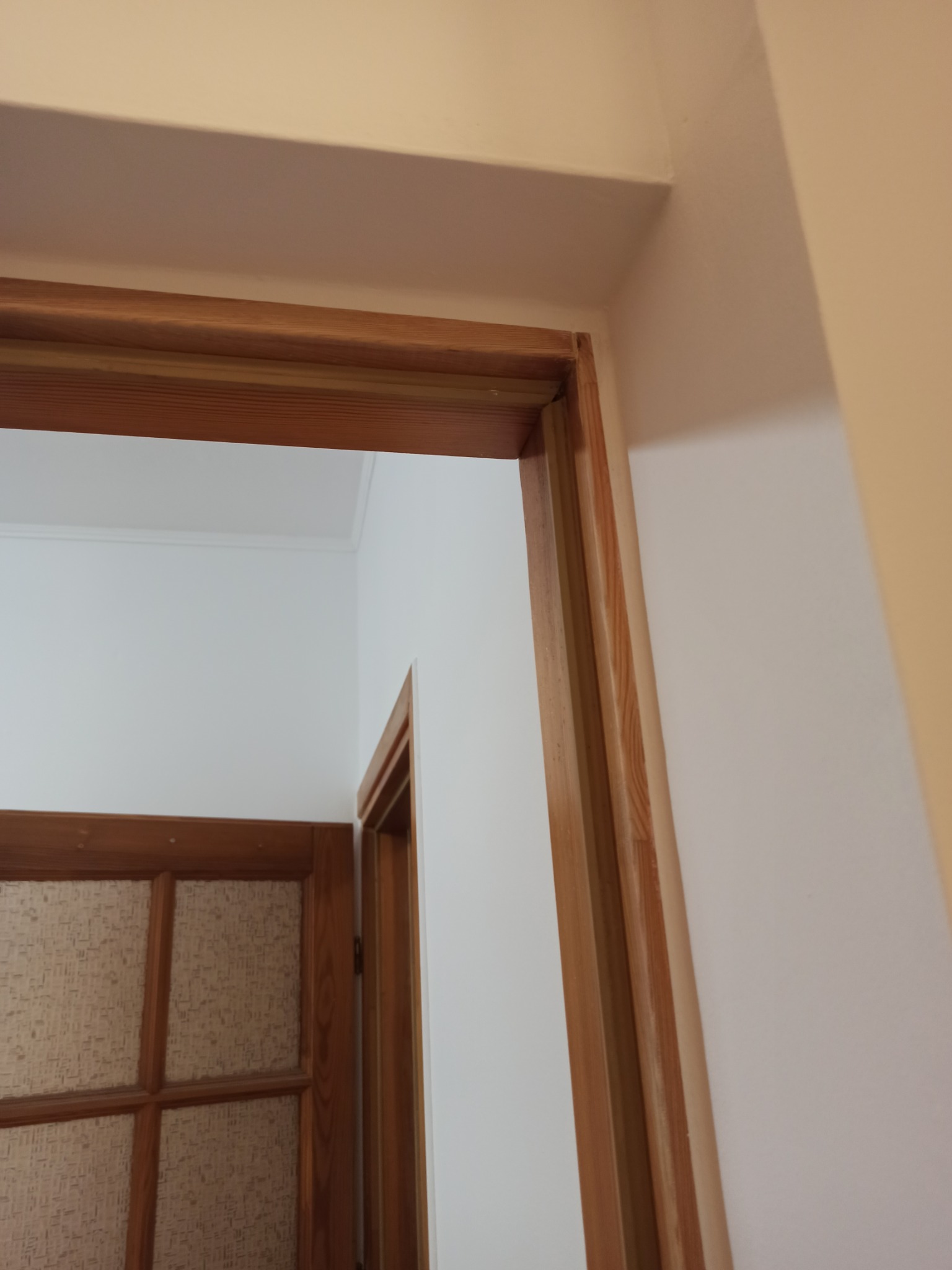 Wnętrze po malowaniu: białe ściany, drewniana futryna drzwiowa i fragment drzwi z szybą. Widok z bliska, skupienie na detalu wykończenia.