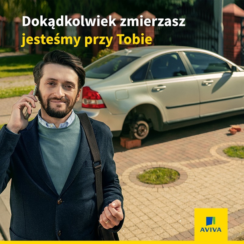 Uśmiechnięty mężczyzna rozmawia przez telefon na tle samochodu bez koła, wspartego na cegłach, z logo firmy ubezpieczeniowej w rogu.