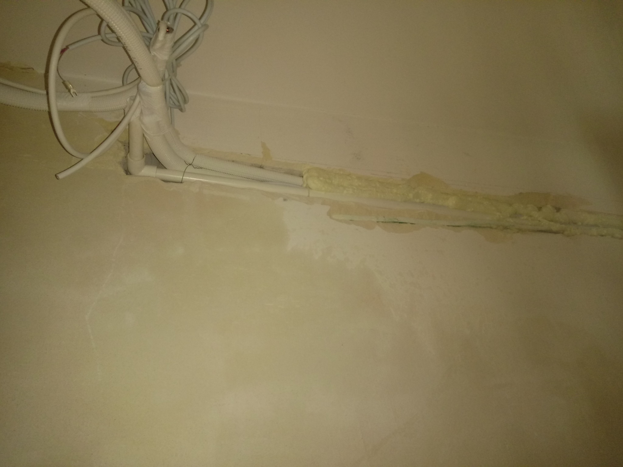 Instalacja przewodów i rur przy ścianie, zabezpieczonych pianką montażową, widoczne przewody elektryczne i rury PCV.