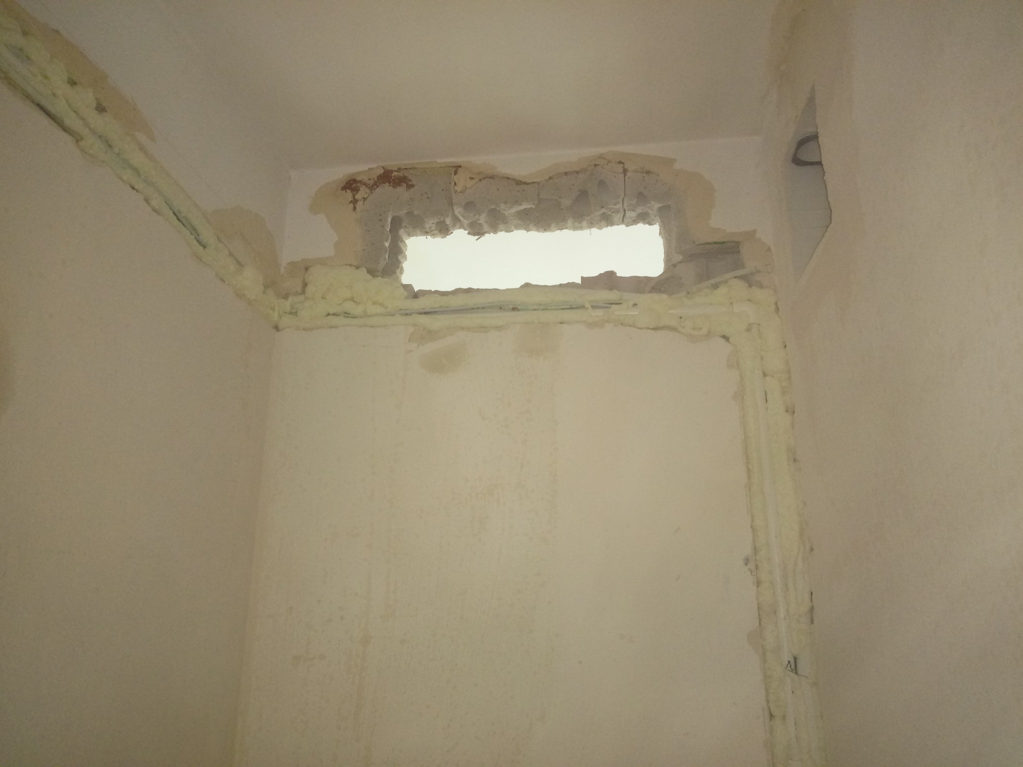 Ściana z wyciętym otworem, zabezpieczonym pianką montażową, widoczne ślady po instalacji rur.