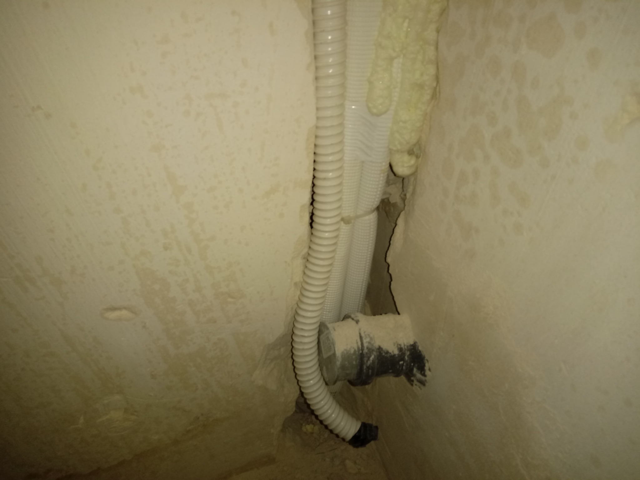 Montaż klimatyzacji: rury wentylacyjne i przewody chłodnicze prowadzone w bruździe w ścianie, zabezpieczone pianką montażową.