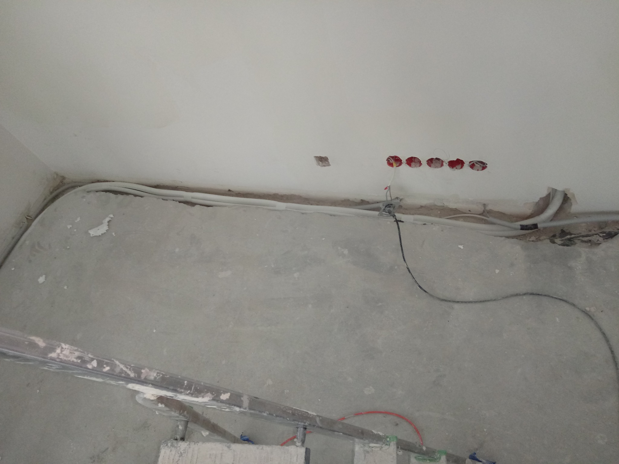 Wnętrze w trakcie remontu: widoczne przewody elektryczne prowadzone wzdłuż ściany pod sufitem, otwory pod gniazdka elektryczne i fragment drabiny malarskiej.