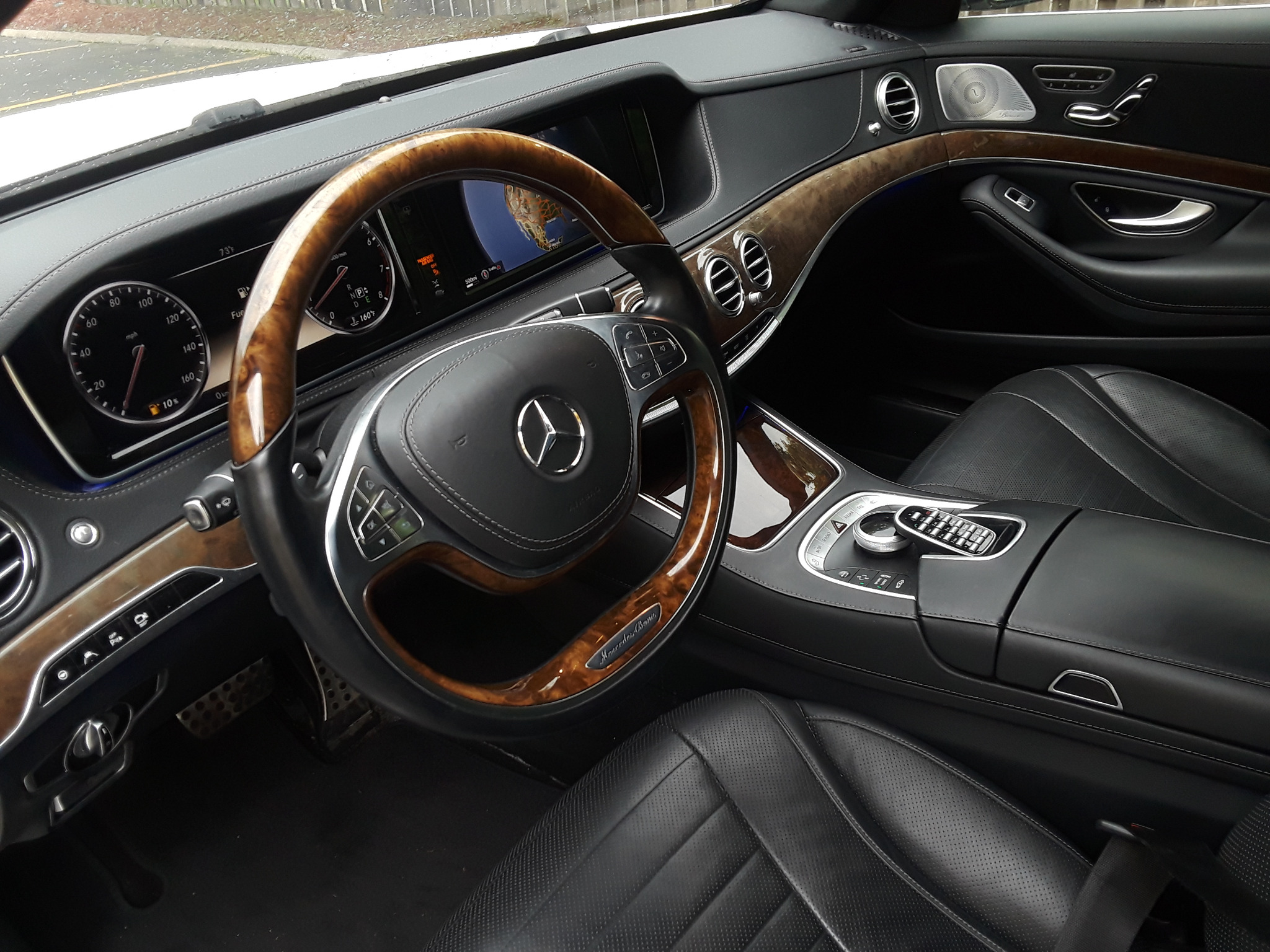 Wnętrze luksusowego samochodu marki Mercedes-Benz z drewnianą kierownicą, czarną skórzaną tapicerką i wyświetlaczem nawigacji.