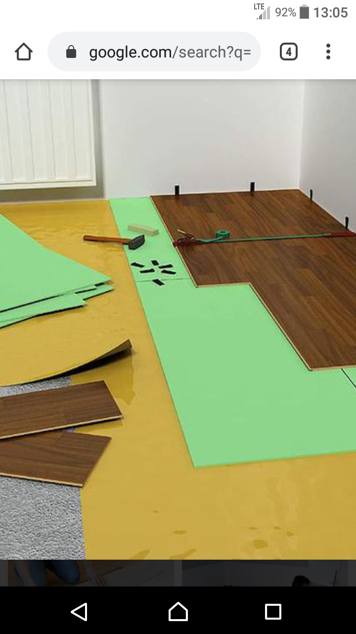 Układanie paneli podłogowych na podkładzie z użyciem młotka i listwy dystansowej, widoczne narzędzia i materiały, częściowo ułożona podłoga.