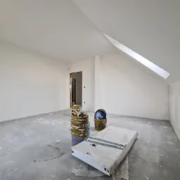 Poddasze po niedawnym malowaniu z widocznymi wiadrami z farbą, narzędziami i nowym grzejnikiem w folii ochronnej, czekającymi na montaż.