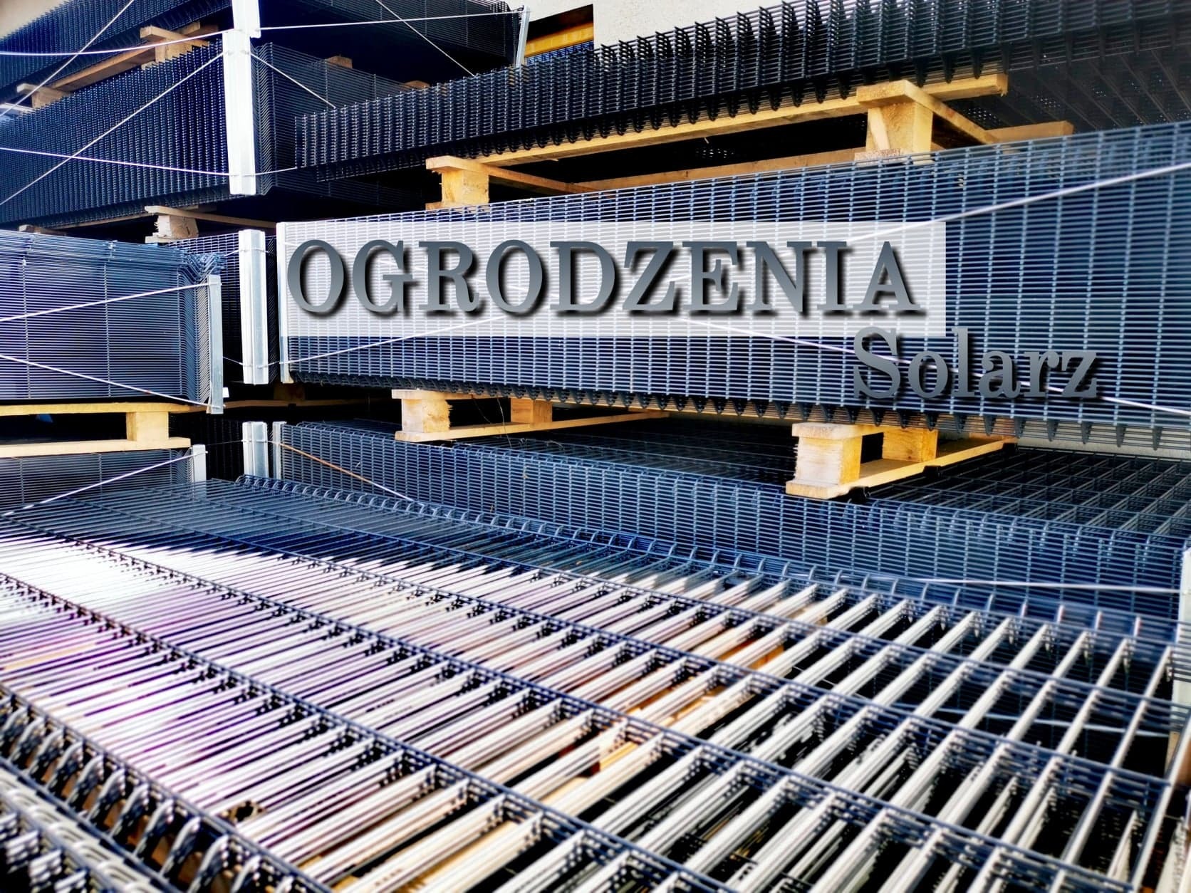 Siatki ogrodzeniowe zgrzewane, ułożone w stosy na drewnianych paletach, z widocznym napisem 'Ogrodzenia Solarz'.
