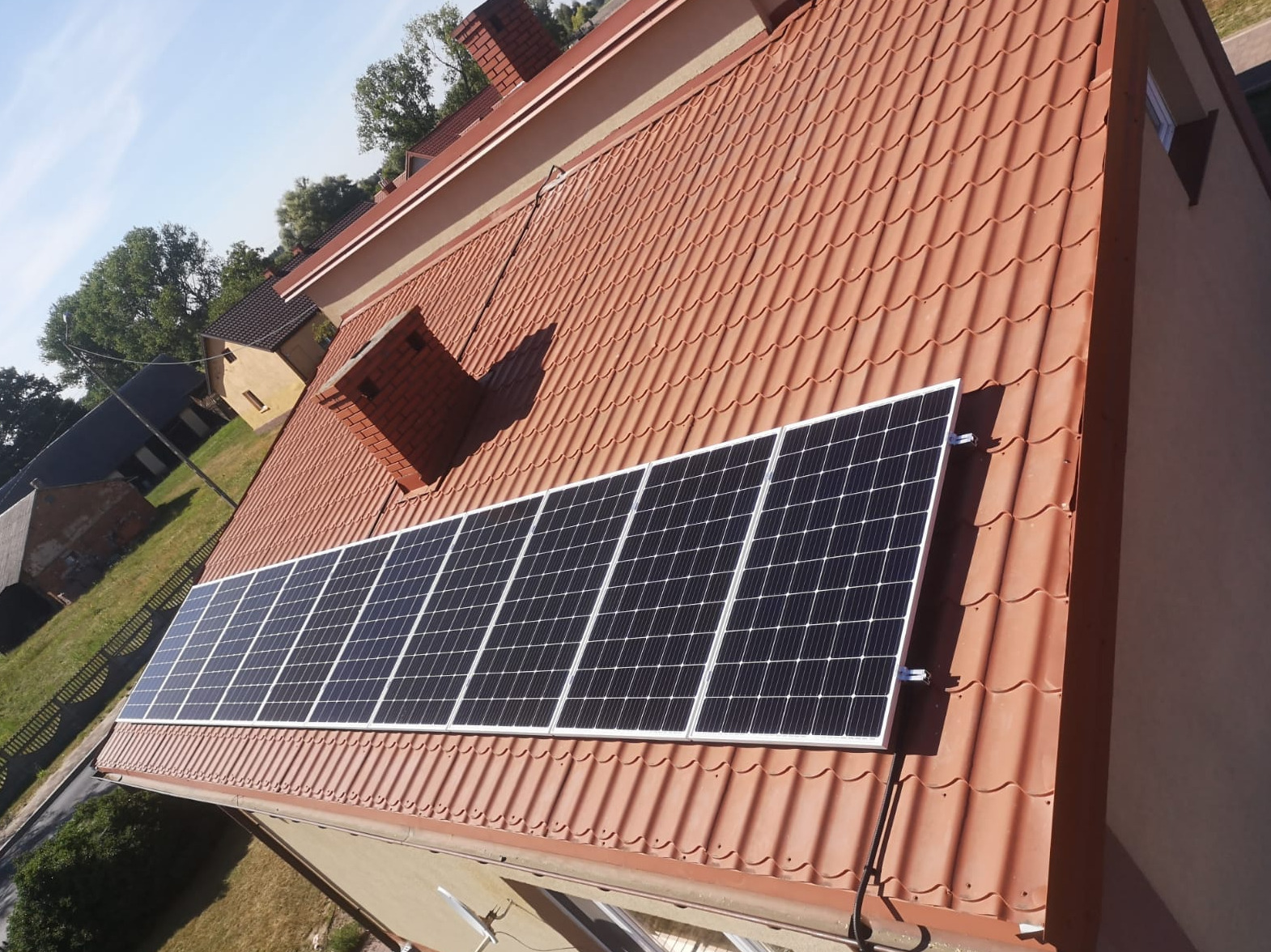 Panel słoneczny zamontowany na dachu z czerwonej dachówki, widok z góry, w tle budynki mieszkalne