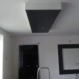 Częściowo pomalowany sufit z wyeksponowaną instalacją elektryczną, widoczna drabina i czarne drzwi w tle, remont w trakcie.