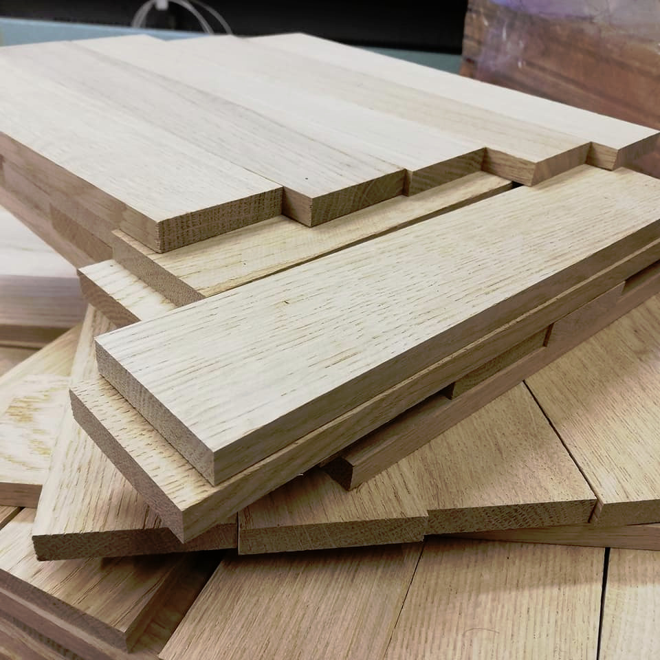 Stos jasnych, drewnianych lameli z widocznym usłojeniem, ułożonych nieregularnie na drewnianej powierzchni.