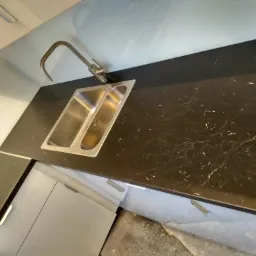 Nowoczesna, dwukomorowa zlewozmywakowa ze stali nierdzewnej w czarnym blacie z marmurkowym wzorem, bateria kuchenna z satynowego metalu, szare szafki kuchenne.