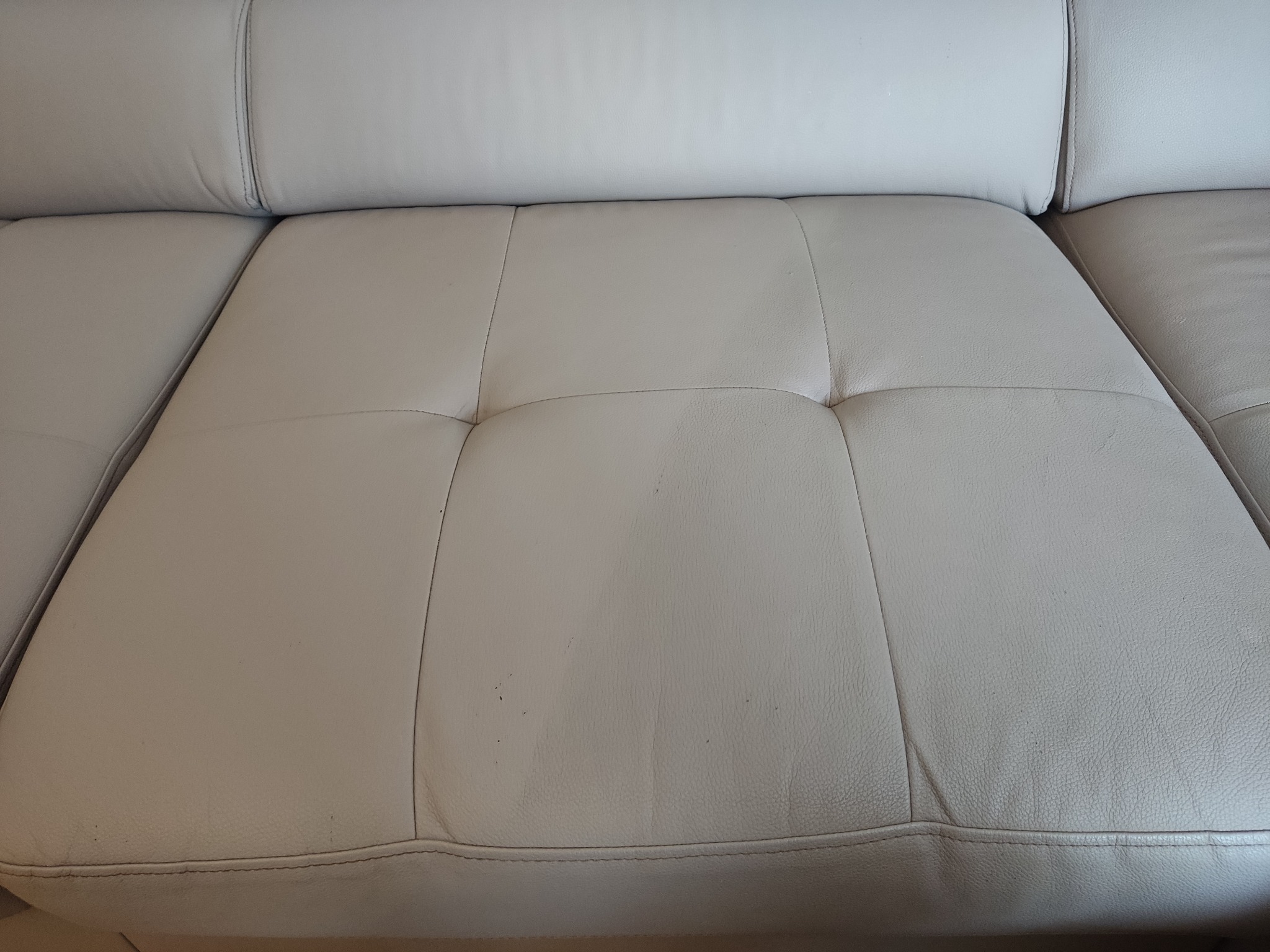 Fragment beżowej, skórzanej kanapy z widocznymi drobnymi zabrudzeniami na siedzisku.