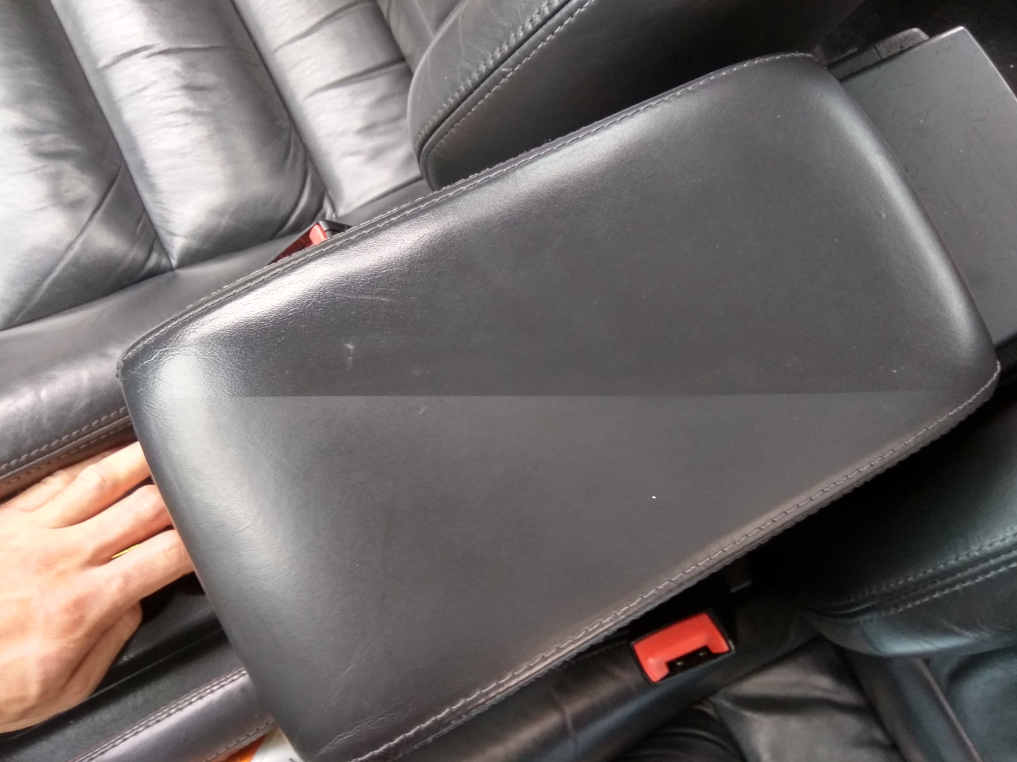 Fragment czarnej skórzanej tapicerki samochodowej z widoczną ręką, ukazujący stan przed czyszczeniem lub naprawą.