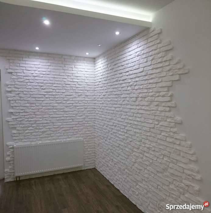 Ściana wykończona dekoracyjną białą cegłą w Olesno, z widocznym grzejnikiem i fragmentem drewnianej podłogi, podświetlona listwą LED w suficie.