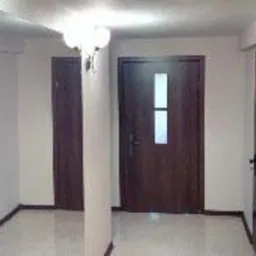 Wnętrze korytarza z trzema ciemnymi drzwiami, oświetlone lampami, widok z perspektywy wejścia.