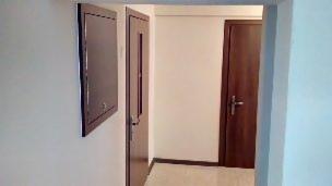 Wnętrze korytarza z dwoma drewnianymi drzwiami i brązową szafką na ścianie, widok z perspektywy wchodzącego.