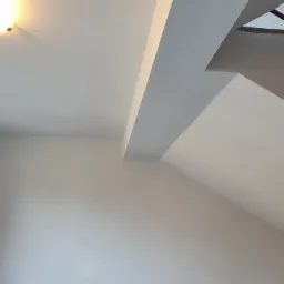 Świeżo pomalowane, jasne wnętrze z widocznym fragmentem sufitu i ściany pod skosem oraz narożnikiem. Widoczna lampa sufitowa w lewym górnym rogu.