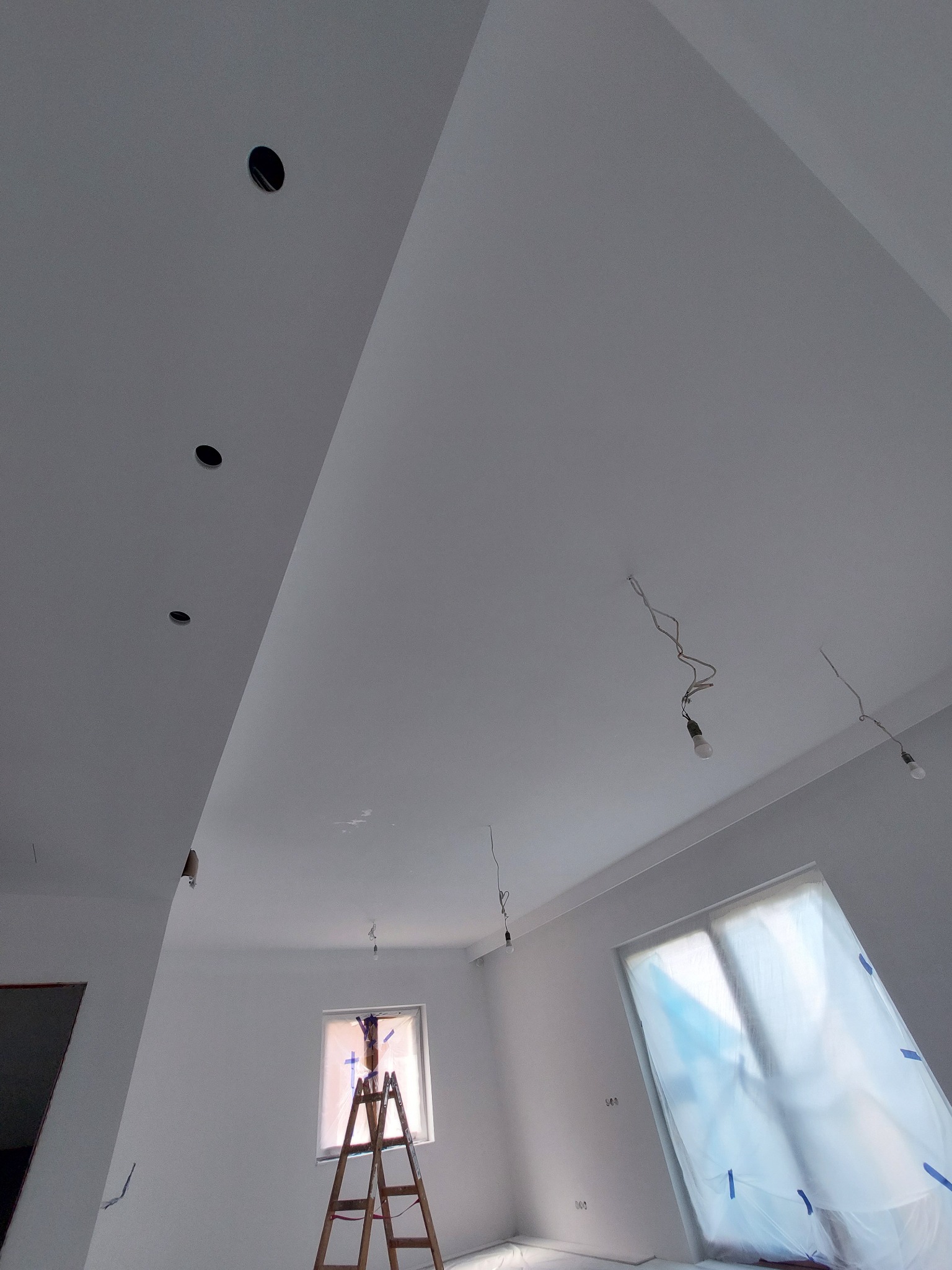 Malowanie wnętrza: widok na sufit z zamontowanymi punktami świetlnymi, ściany i okna zabezpieczone folią malarską, drewniana drabina ustawiona pod oknem.