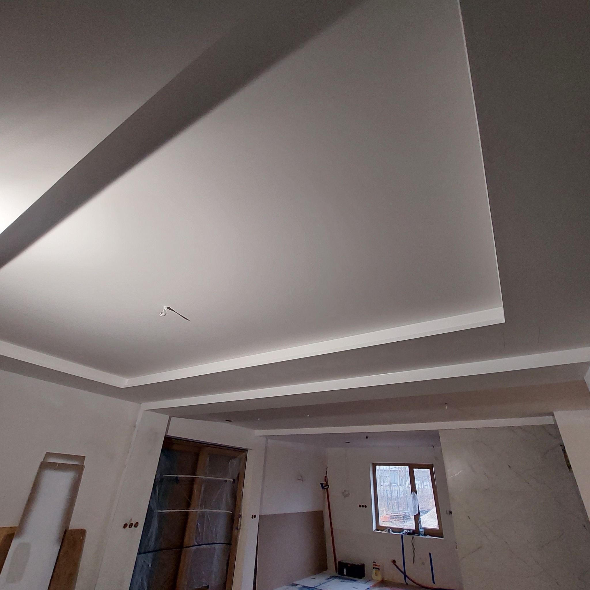 Nowoczesny sufit podwieszany z oświetleniem LED w trakcie montażu, widoczne niedokończone ściany i okno w tle.