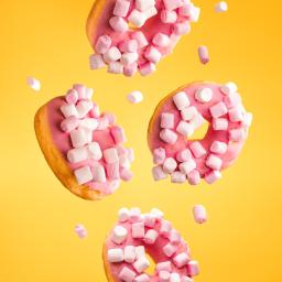 Design Space - Trzy pączki z różowym lukrem i piankami marshmallow w locie na żółtym tle, oświetlone studyjnym światłem.