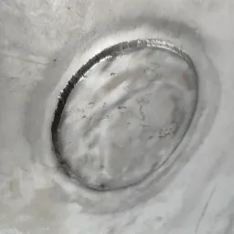 Zbliżenie na spoinę okrągłą na metalowej powierzchni, widoczne ślady po spawaniu, szary odcień metalu, delikatne nierówności.