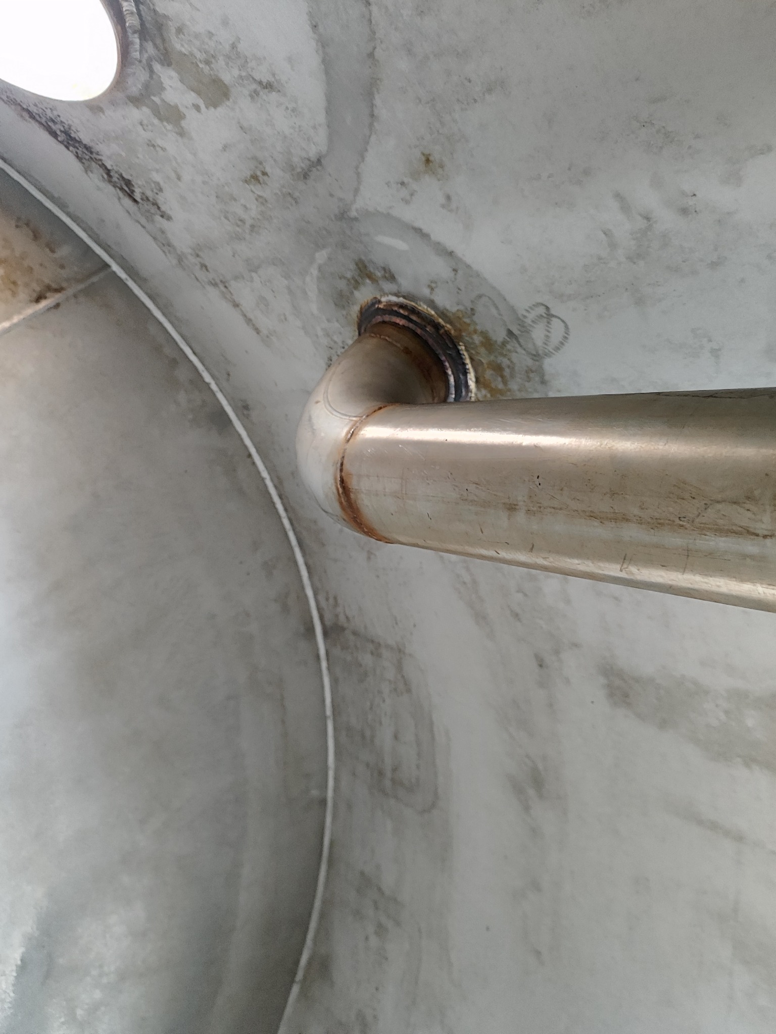 Wnętrze metalowej konstrukcji z przyspawaną rurą, widok z dołu. Widoczne ślady spawania i niedoskonałości powierzchni.