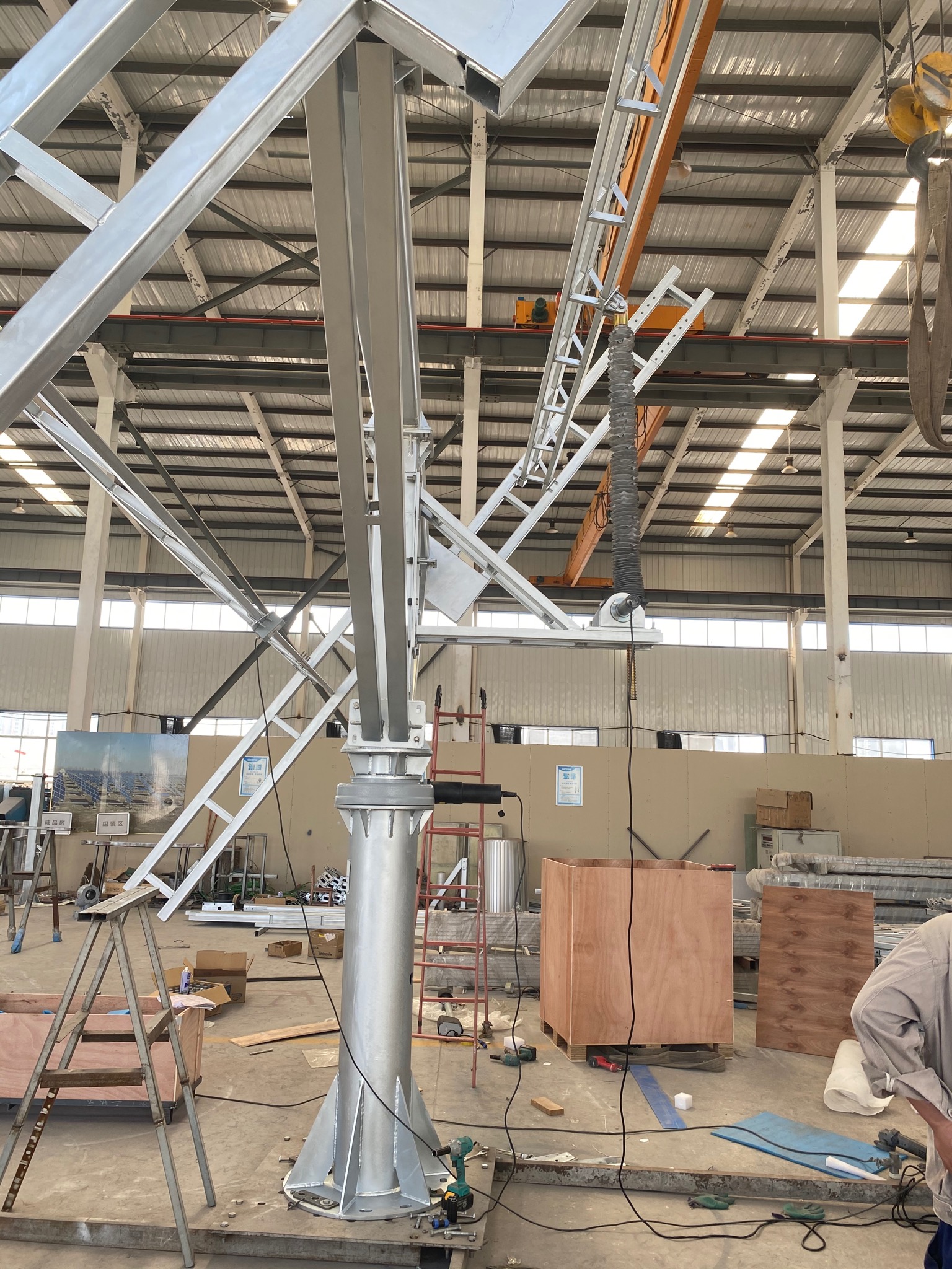 Metalowa konstrukcja wsporcza w hali produkcyjnej, prawdopodobnie element systemu montażowego, z widocznymi narzędziami i elementami mocującymi na podłodze.