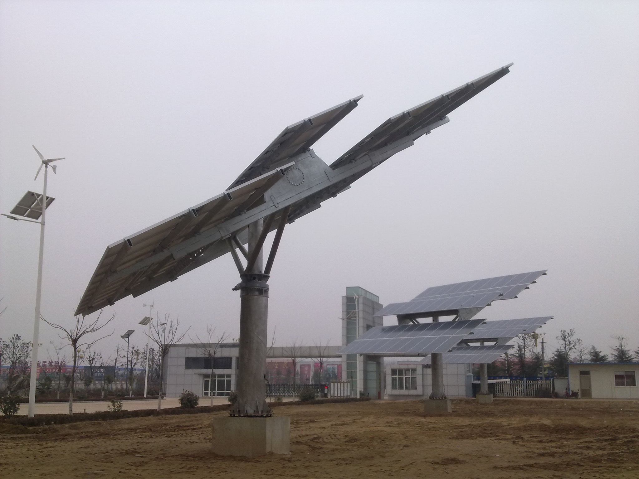 Futurystyczna instalacja paneli słonecznych na metalowym stelażu, z turbiną wiatrową w tle, w pochmurny dzień.