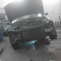 Samochód z otwartą maską, podniesiony na podnośniku w warsztacie, z widocznymi narzędziami na podłodze.