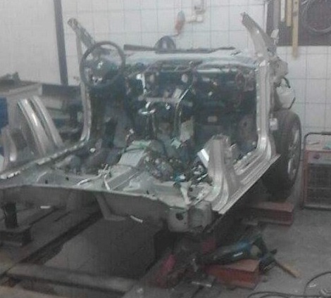 Zdjęcie szkieletu samochodu w warsztacie, widoczne elementy wnętrza i karoserii, narzędzia leżące na podłodze, wnętrze w trakcie naprawy lub rozbiórki.