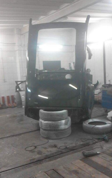 Kabinę ciężarówki w trakcie naprawy, podparta stosem opon w warsztacie.