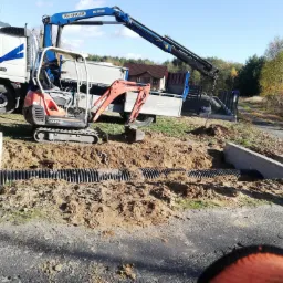 Ciężarówka z dźwigiem i minikoparką przy wykopie z ułożonymi rurami drenażowymi, Widełka. W tle dom i drzewa.
