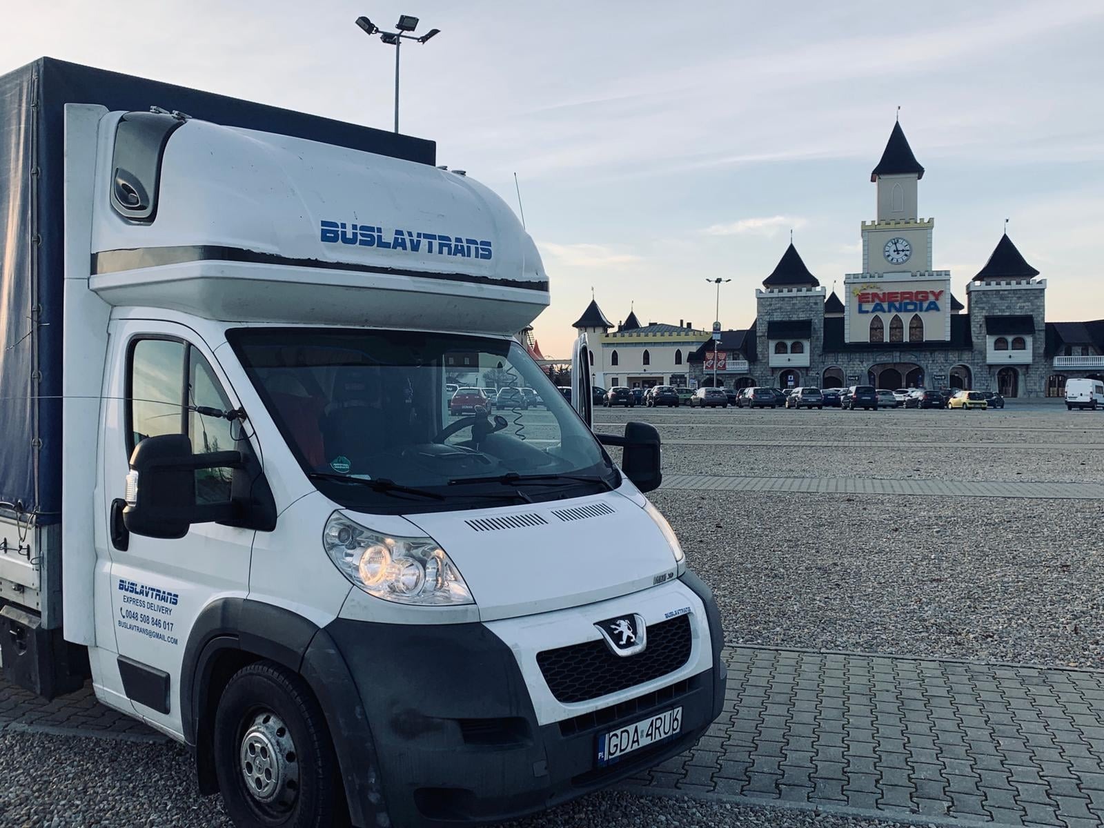 Biały bus z napisem BUSLAVTRANS na tle Energylandii w Zatorze, rejestracja z Gdańska, widok z boku.