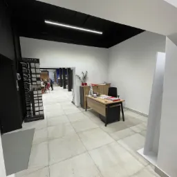 Wnętrze salonu z ekspozycją paneli podłogowych Mardom Decor, jasna podłoga z płytek, biurko z krzesłem i rośliny doniczkowe w tle.