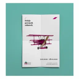 Plakat reklamowy wystawy w Muzeum Zabawek i Zabawy, prezentujący fioletowy model samolotu dwupłatowego na białym tle z datami i adresem muzeum.