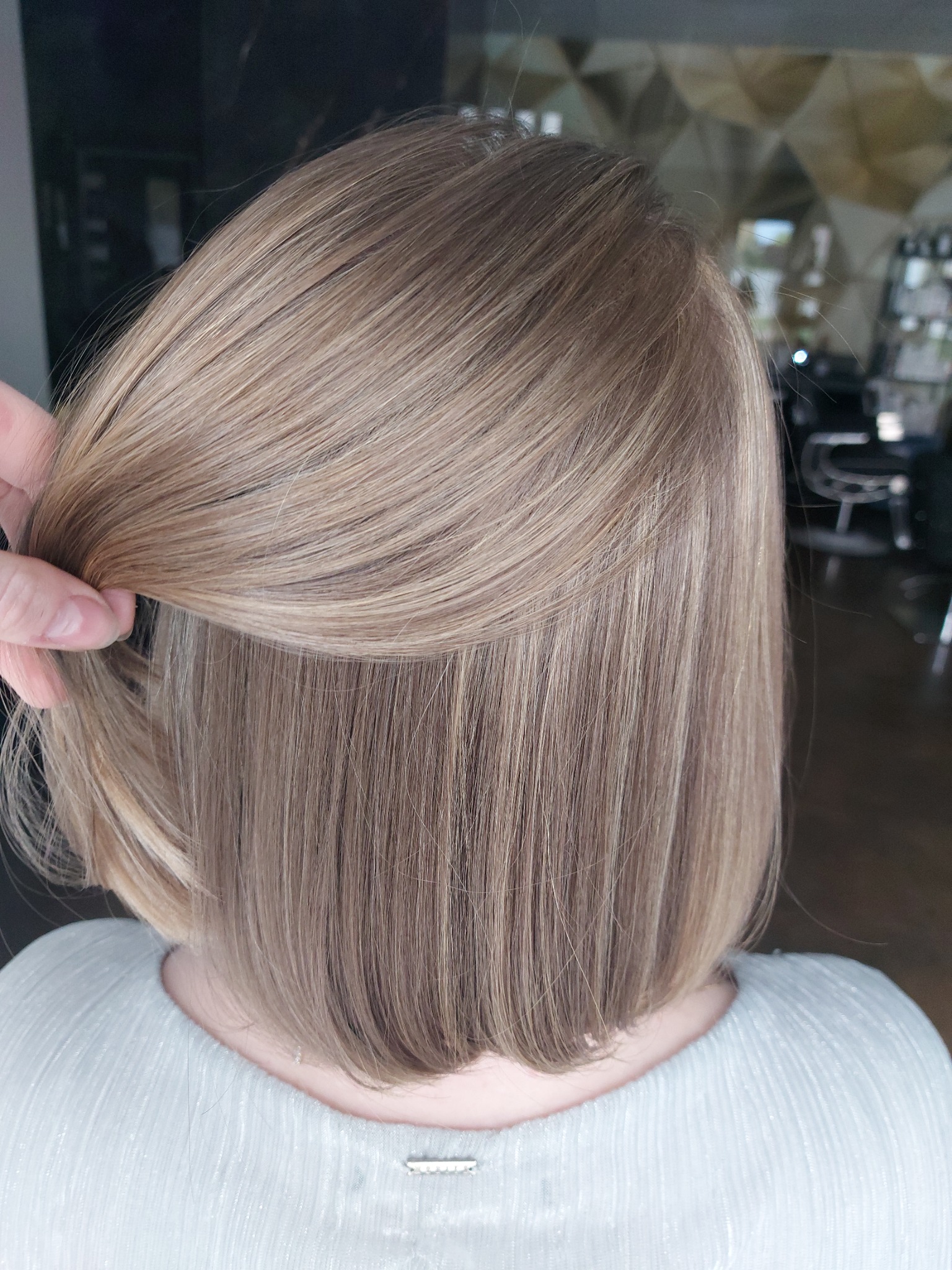 Wyprostowane, blond włosy o długości do ramion, z pasmem podnoszonym palcami, ukazujące gładką teksturę i subtelne refleksy.
