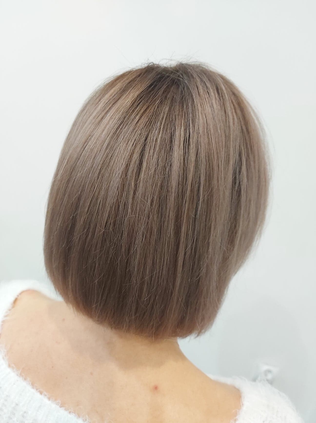 Krótkie, proste cięcie w odcieniach popielatego blondu, widok z tyłu, biały sweter.