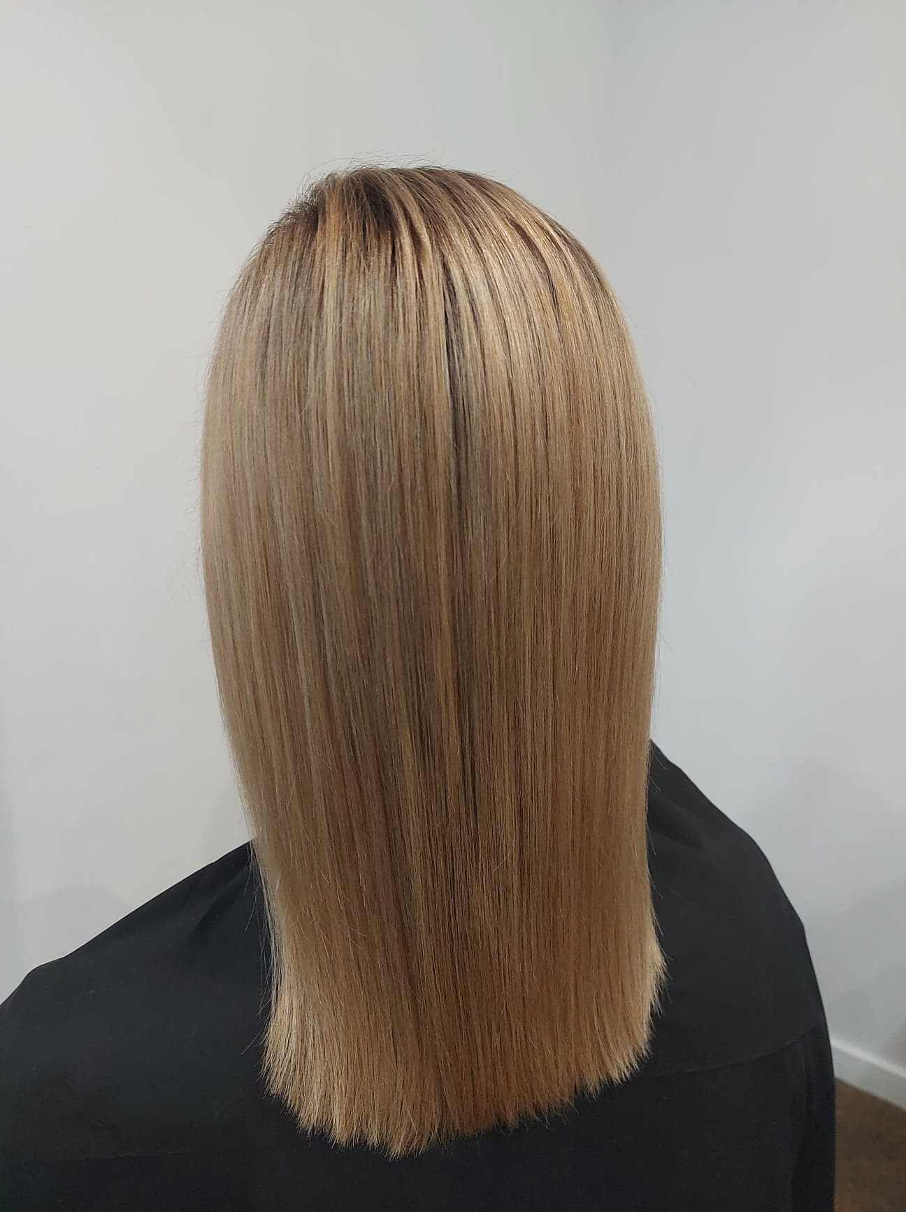 Proste, blond włosy do ramion, z delikatnym odrostem u nasady, widok z tyłu, na czarnym tle peleryny.