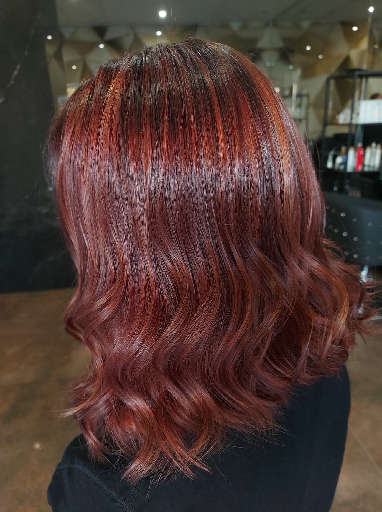 Ciemnoczerwone, falowane włosy z refleksami, widok z tyłu, profesjonalne oświetlenie salonowe.