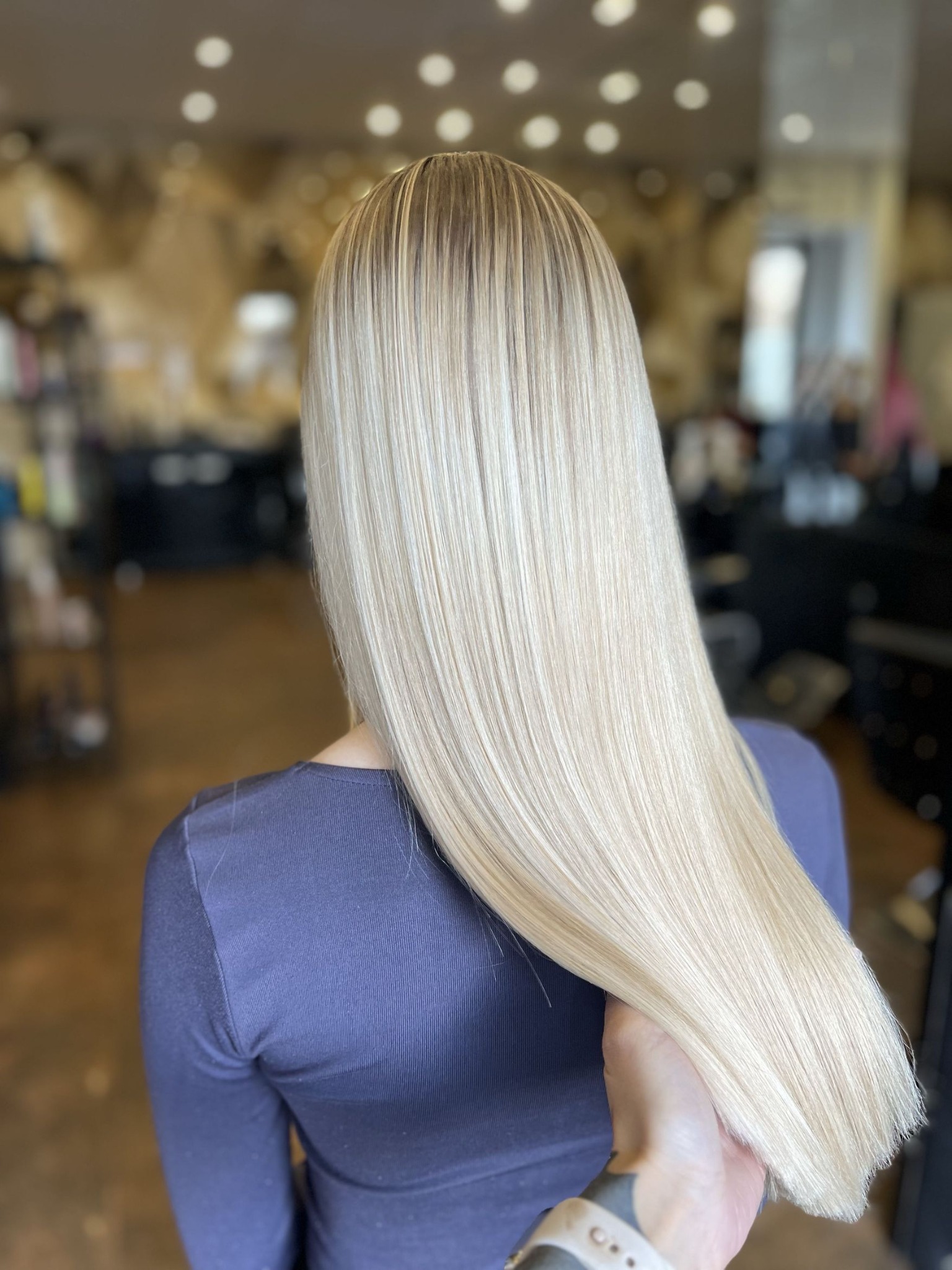 Blond włosy po koloryzacji z widocznymi odrostami w ciemniejszym kolorze, trzymane przez dłoń w salonie fryzjerskim.