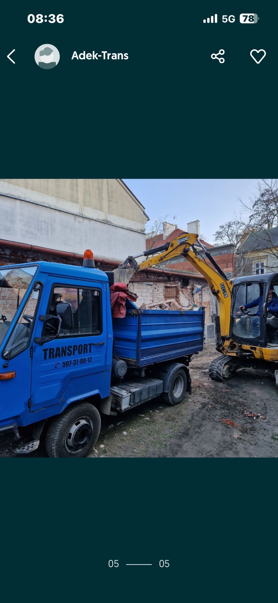 Niebieska laweta z napisem 'TRANSPORT' i numerem telefonu, załadowana gruzem, obok żółta minikoparka JCB podczas załadunku na tle ceglanego budynku.