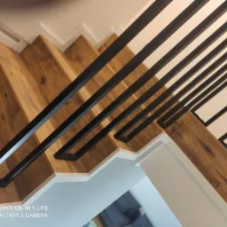 Schody z drewnianymi stopniami i nowoczesną balustradą z czarnych, prostokątnych profili, widok z góry, jasne, minimalistyczne wnętrze.