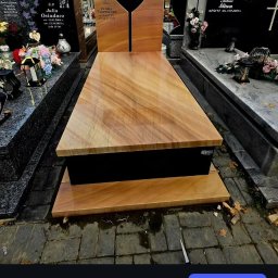 Kamieniarstwo Bieleccy - Jasny, drewnopodobny nagrobek z wyciętym sercem i zdjęciem osoby zmarłej, na tle innych nagrobków na cmentarzu. Widoczne detale wykończenia i faktura kamienia.