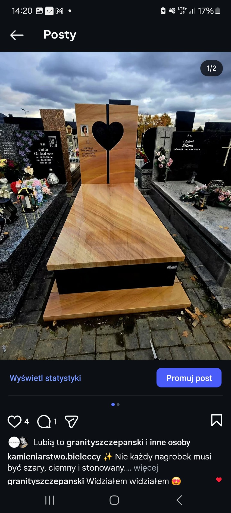 Jasny, drewnopodobny nagrobek z wyciętym sercem i zdjęciem osoby zmarłej, na tle innych nagrobków na cmentarzu. Widoczne detale wykończenia i faktura kamienia.