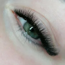 Zielone oko z gęstymi, czarnymi, sztucznymi rzęsami, widoczne delikatne załamania skóry wokół oka.