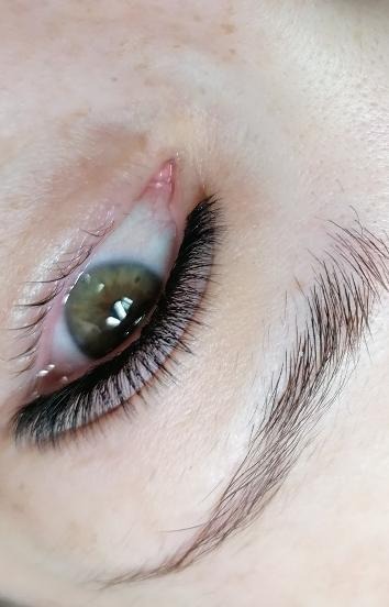 Zbliżenie na oko z przedłużonymi, gęstymi, czarnymi rzęsami; widoczna brązowa tęczówka i naturalne brwi.