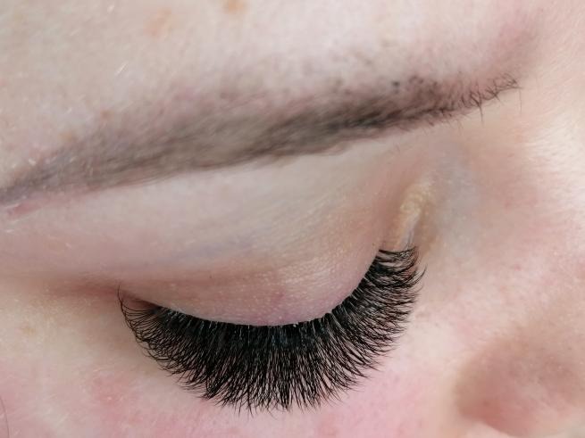 Zbliżenie na oko z gęstymi, czarnymi, profesjonalnie przedłużonymi rzęsami, widoczna delikatna skóra powieki i brwi.