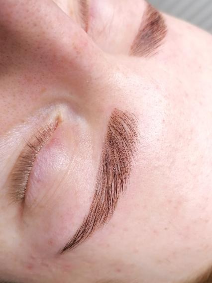 Makro zbliżenie na brwi po zabiegu microbladingu, widoczne pojedyncze włoski pigmentu i naturalne włoski, skóra z drobnymi niedoskonałościami.