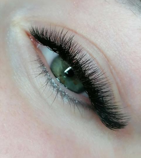 Zielone oko z gęstymi, czarnymi, sztucznymi rzęsami, widoczne delikatne załamania skóry wokół oka.