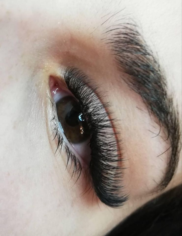 Zbliżenie na oko z brązową tęczówką i gęstymi, przedłużonymi czarnymi rzęsami; widoczna struktura skóry powiek i brwi.